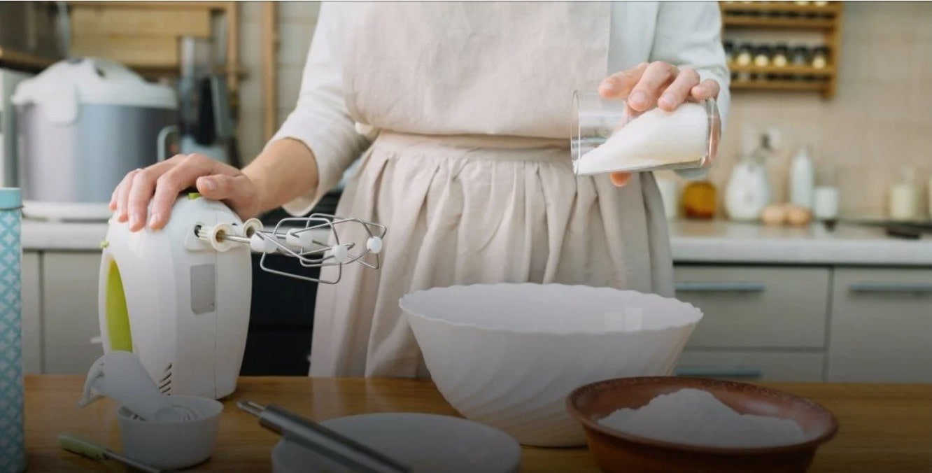 Woman in beige apron and white dress pouring milk